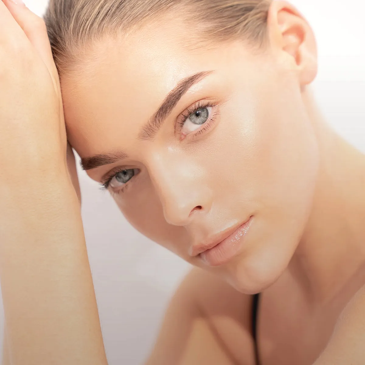 NEWSHA Beauty-Motiv mit blonden, zurückgestylten Haaren, strahlendem Hautglanz, hellen Augen und natürlichem Look vor hellem Hintergrund.