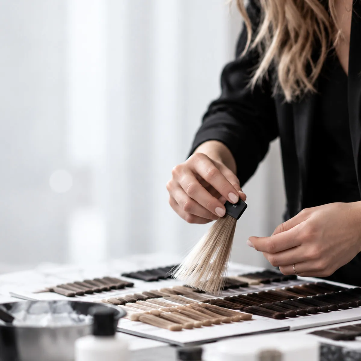 Professionelle Haarcoloration mit verschiedenen Haarfarbnuancen: Eine Friseurin vergleicht blonde Haarsträhnen anhand einer Farbkarte im Salon.