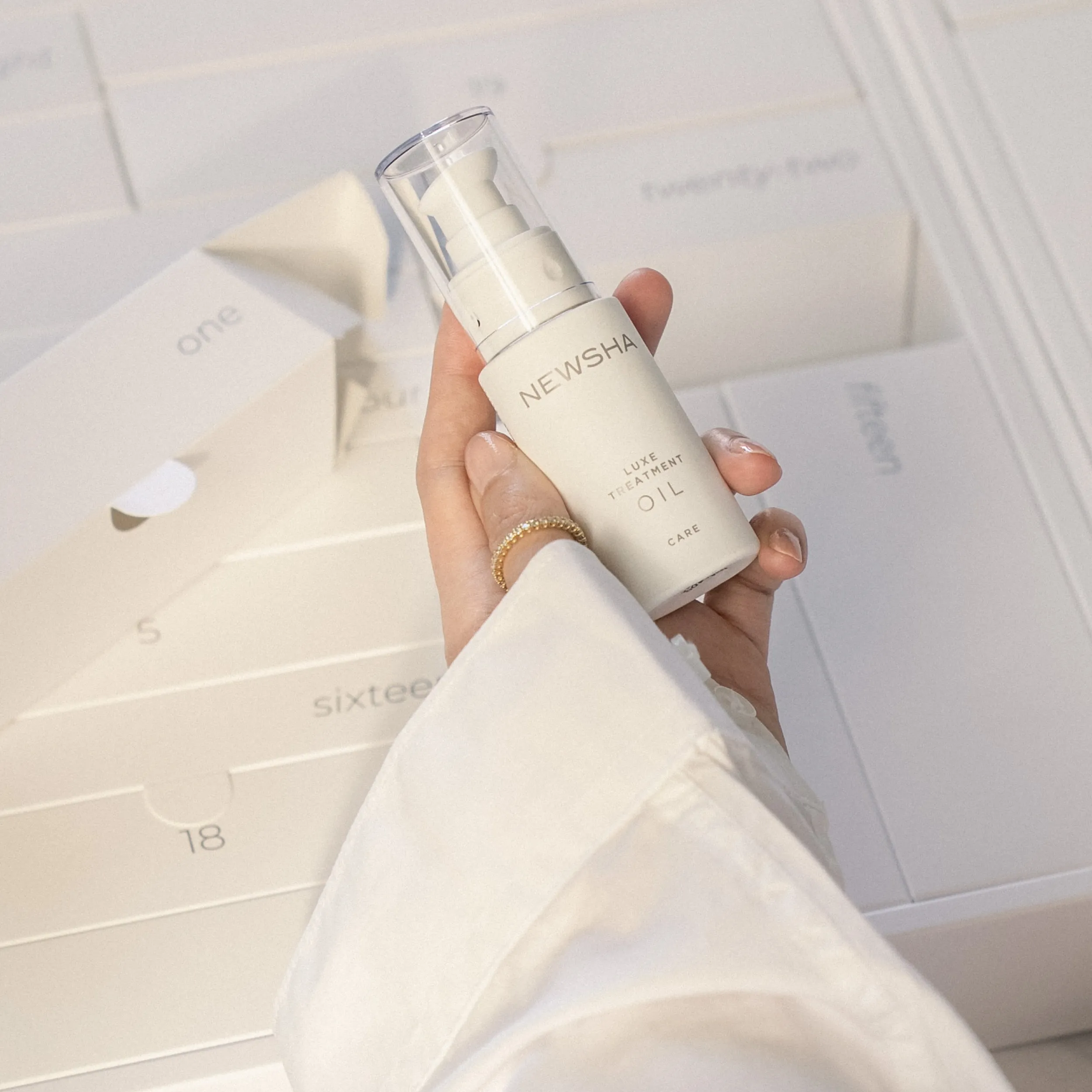 Hand hält das NEWSHA Luxe Treatment Oil über einem geöffneten NEWSHA Adventskalender mit nummerierten Fächern.