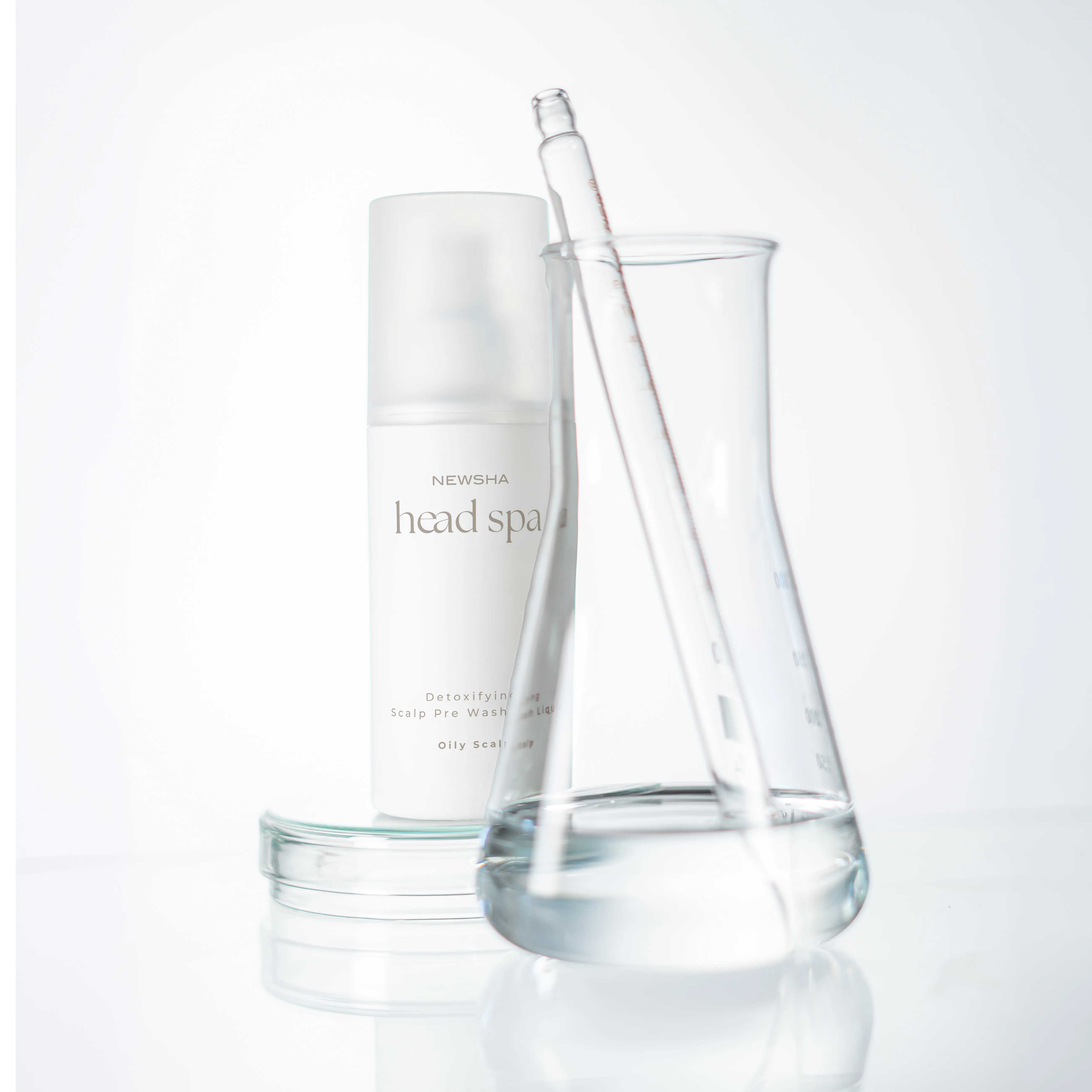 NEWSHA Head Spa Detoxifying Scalp Pre Wash Liquid f&uuml;r fettige Kopfhaut neben einem transparenten Laborgef&auml;&szlig; mit Fl&uuml;ssigkeit und Glaspipette.