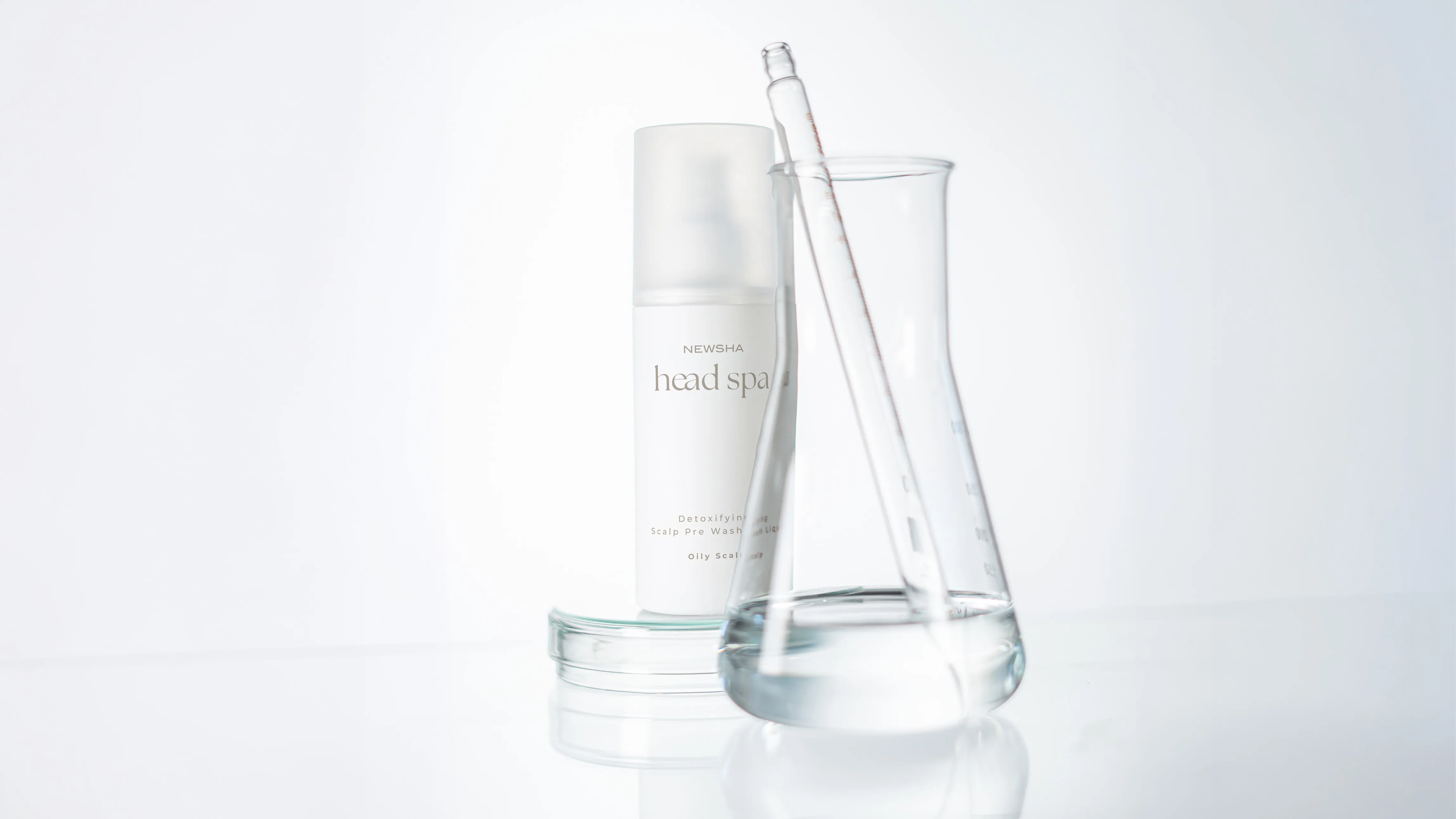 NEWSHA Head Spa Detoxifying Scalp Pre Wash Liquid f&uuml;r fettige Kopfhaut neben einem transparenten Laborgef&auml;&szlig; mit Fl&uuml;ssigkeit und Glaspipette.