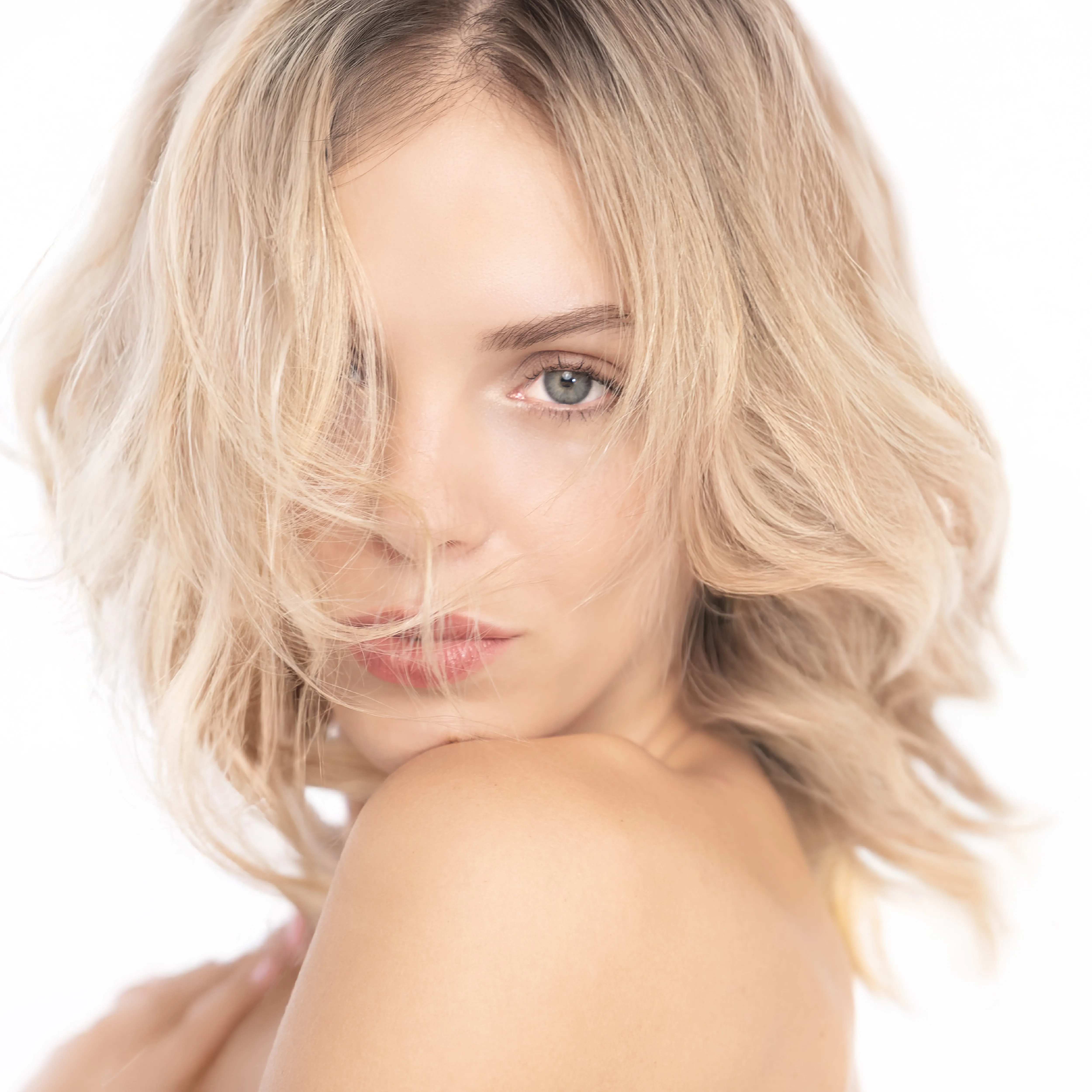 Blonde Frau mit volumin&ouml;sem Bob und nat&uuml;rlichem Make-up auf hellem Hintergrund.