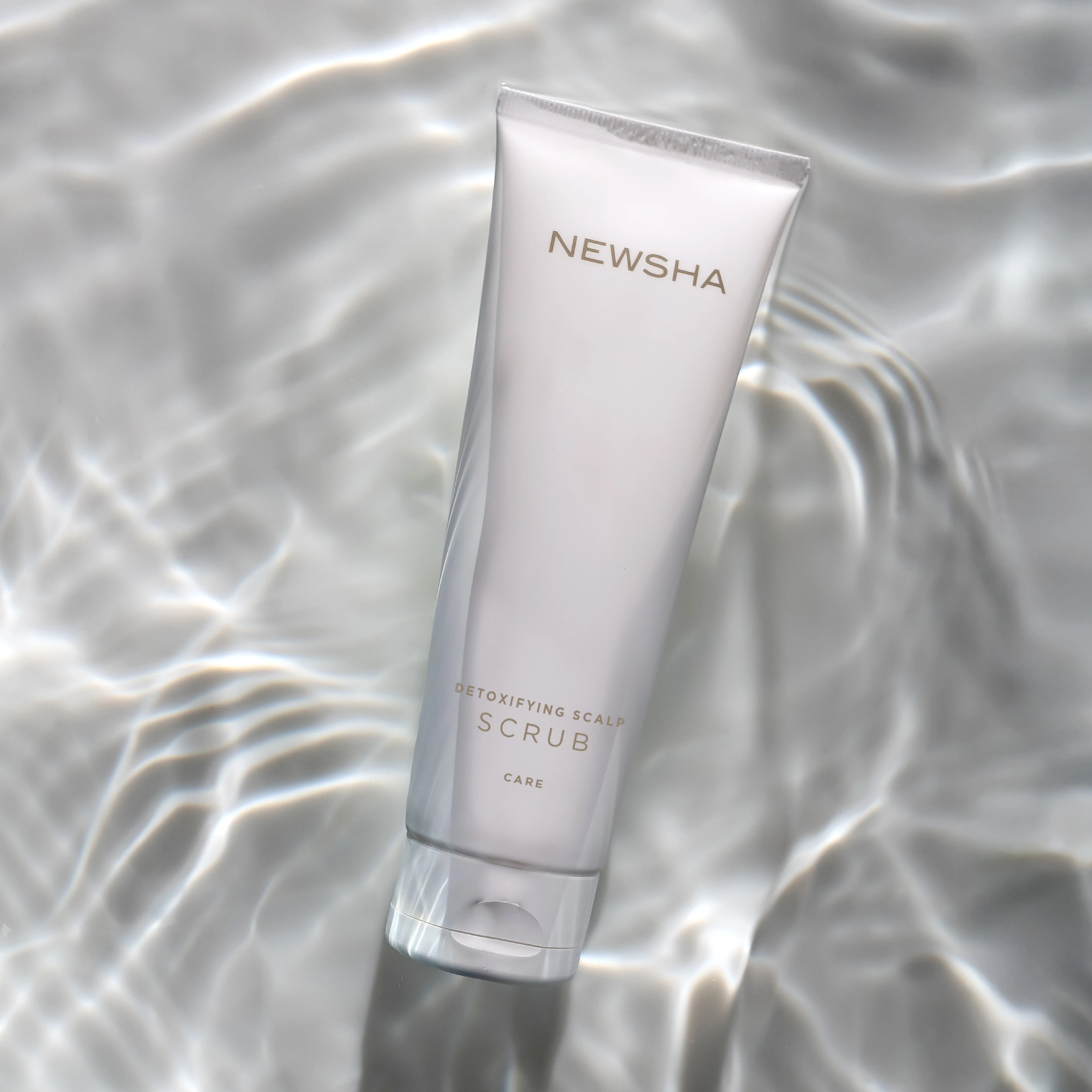 Detoxifying Scalp Scrub Tube auf reflektierendem Wasserhintergrund inszeniert.