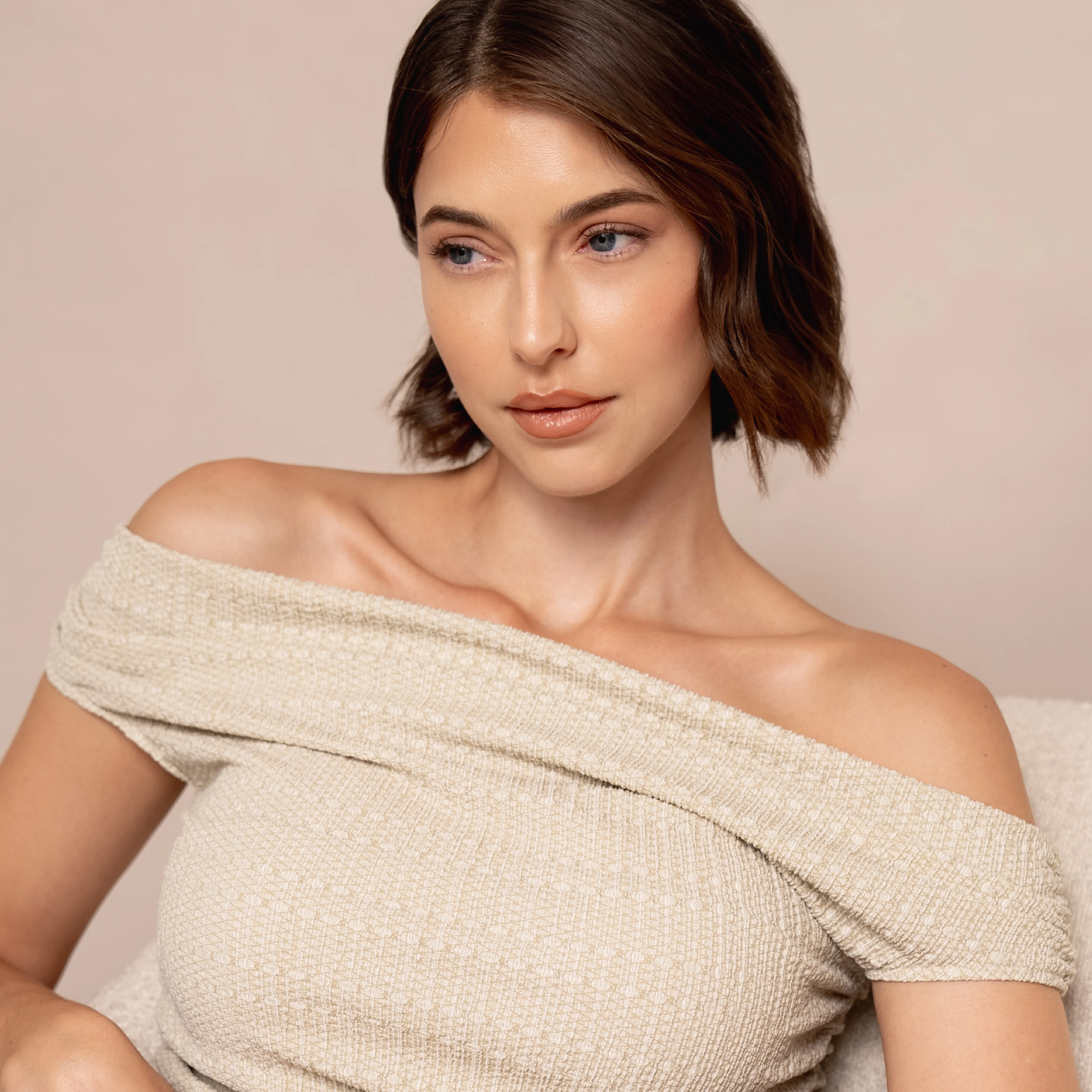 Frau mit kurzem Bob und elegantem Off-Shoulder-Look vor neutralem Hintergrund.