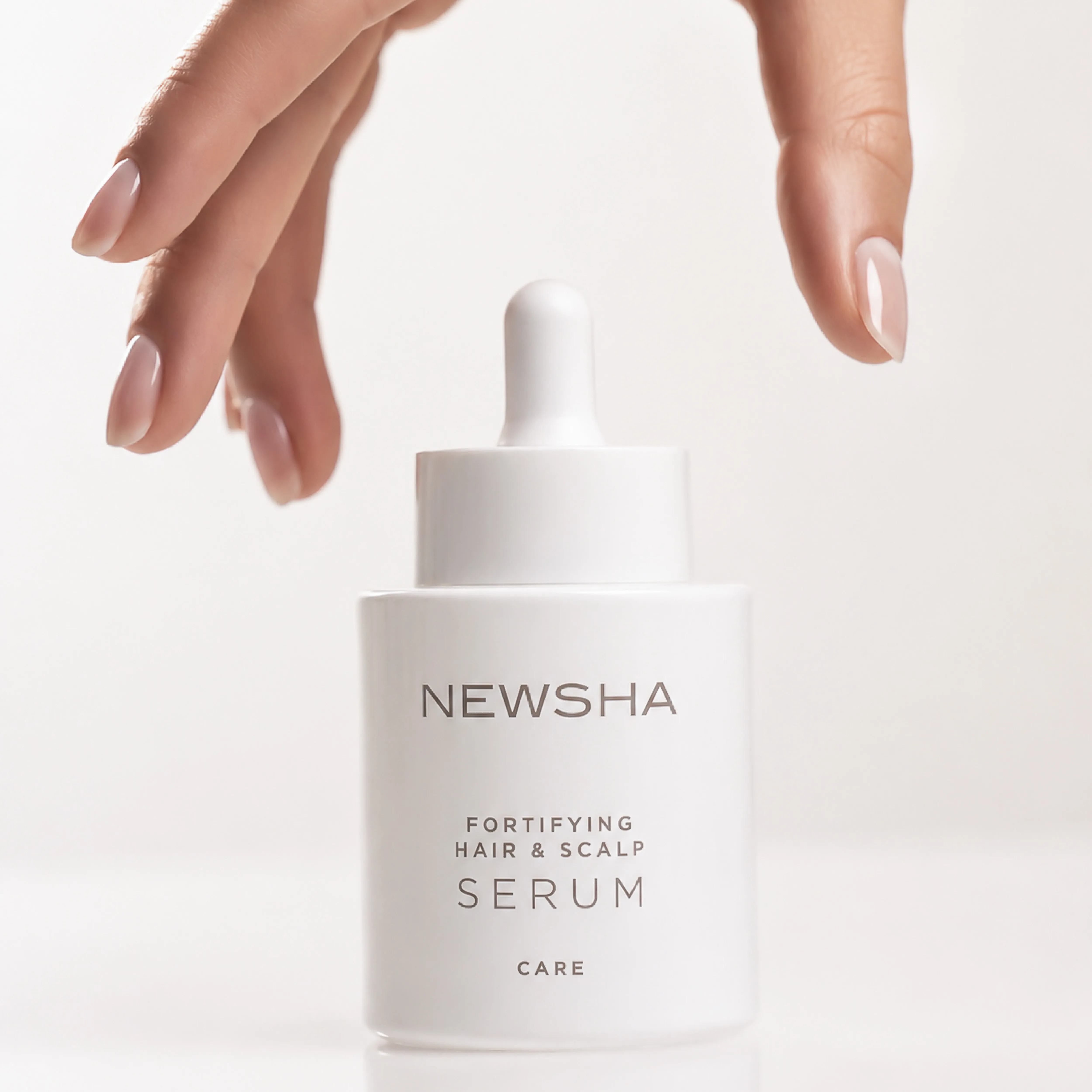 NEWSHA Fortifying Hair & Scalp Serum mit Pipette, umrahmt von gepflegten H&auml;nden vor hellem Hintergrund.