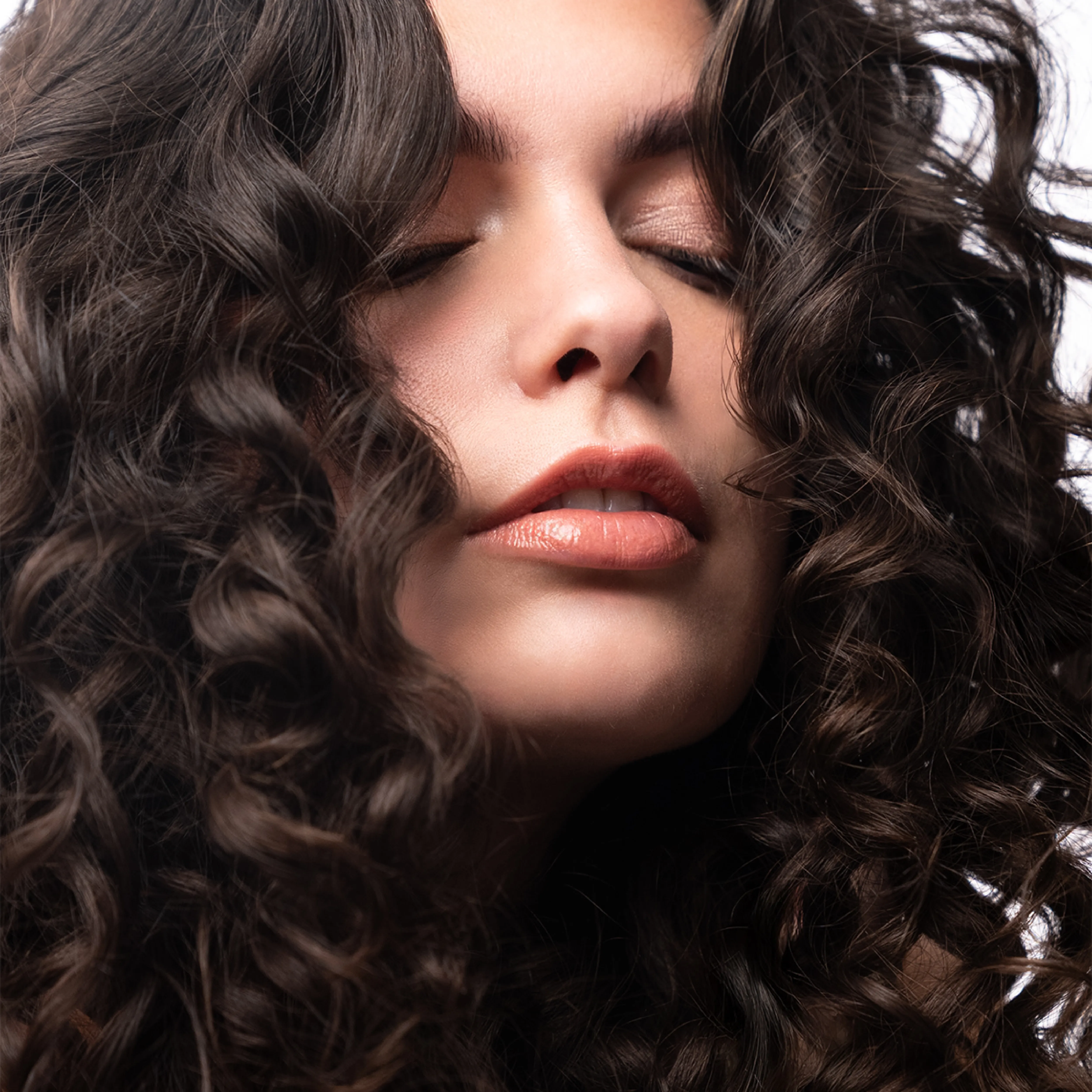 Frau mit definierten dunklen Locken und geschlossenen Augen vor hellem Hintergrund.