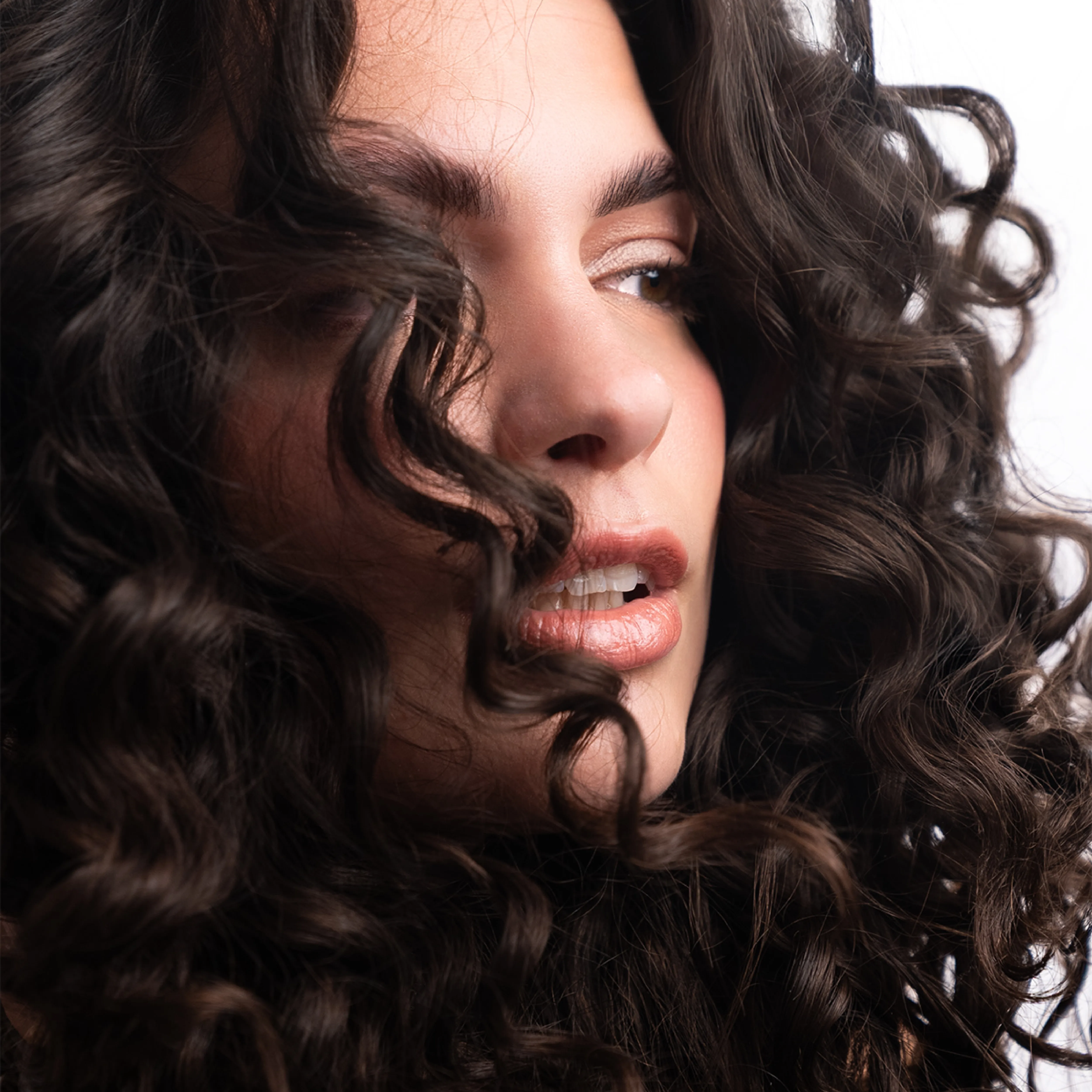 Portrait einer Frau mit volumin&ouml;sen, definierten dunklen Locken und nat&uuml;rlichem Make-up.