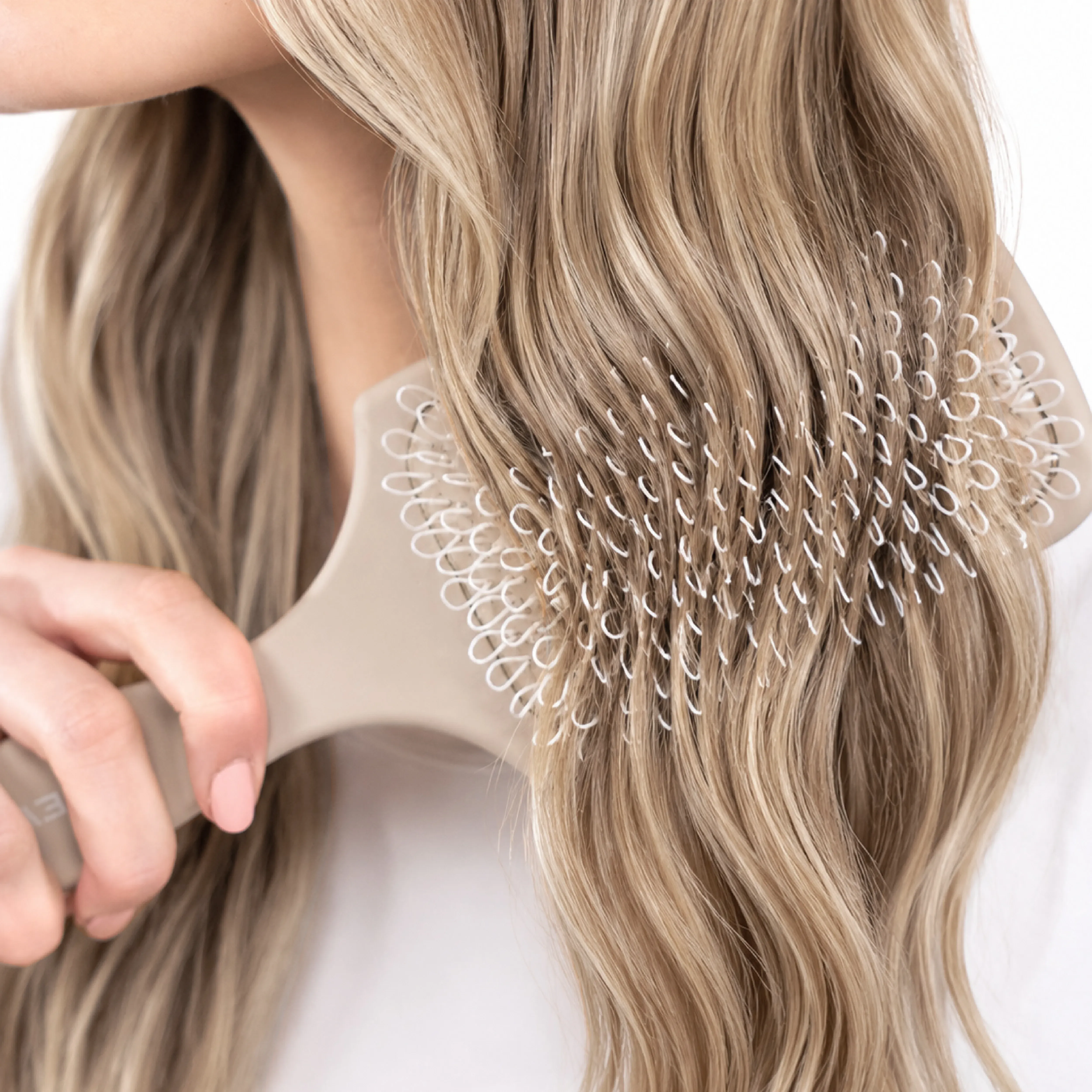 Blonde gewellte Haare werden mit einer NEWSHA Paddle Brush sanft ausgeb&uuml;rstet.