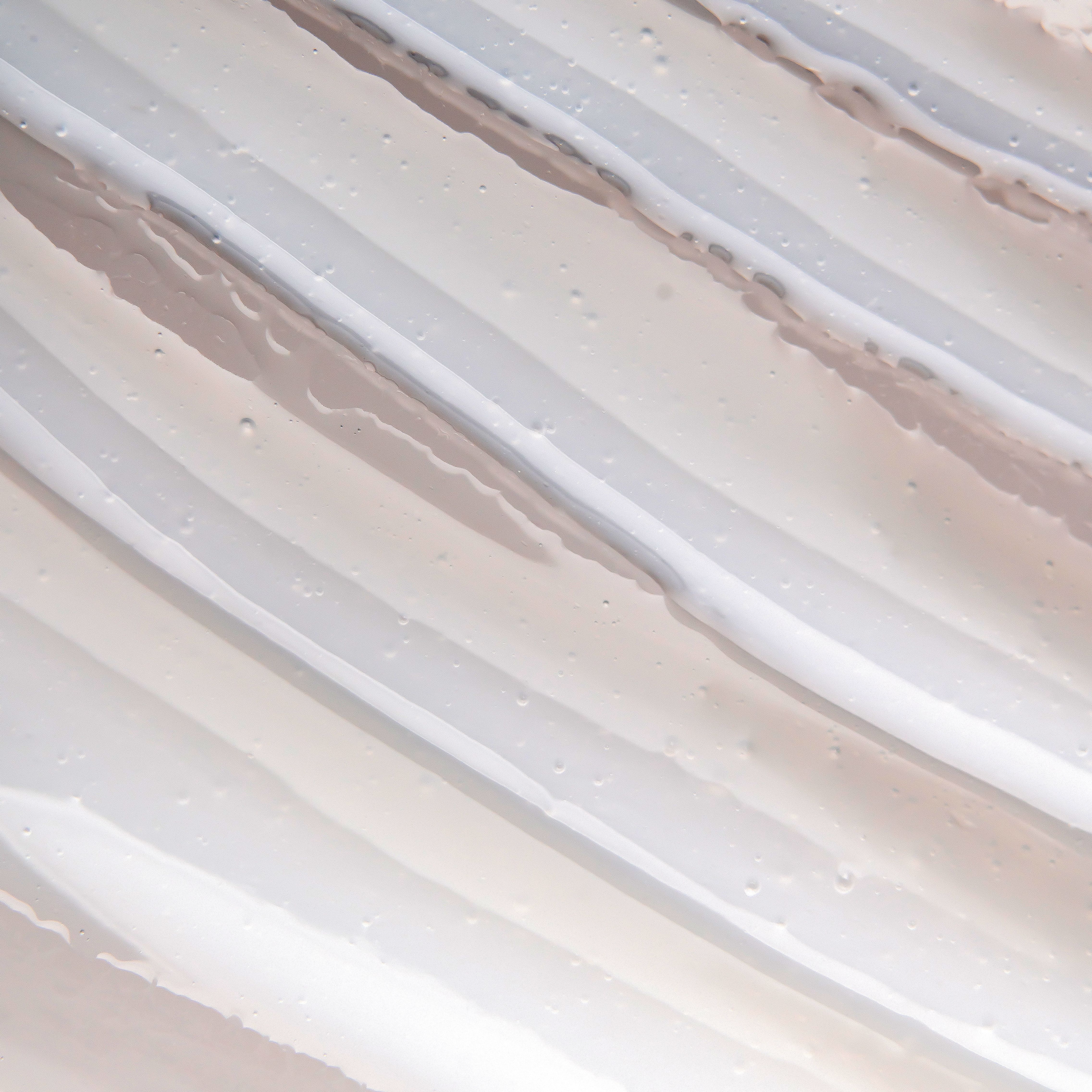 Strukturierte Creme-Textur mit gleichmäßigen Rillen und glänzenden Details auf einem hellen, cleanen Hintergrund.