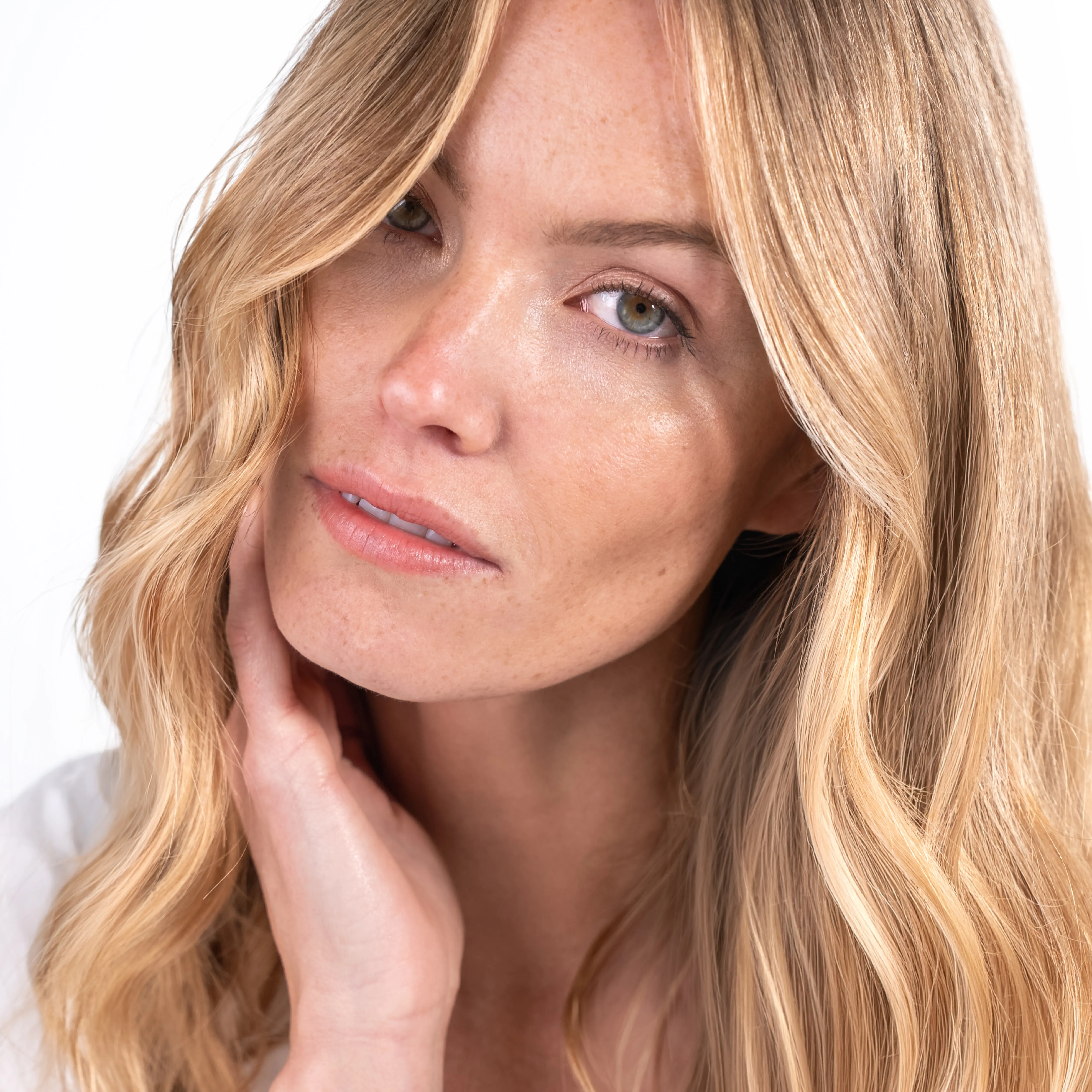 Portrait einer blonden Frau mit weichen Wellen und natürlichem Glow auf hellem Hintergrund.