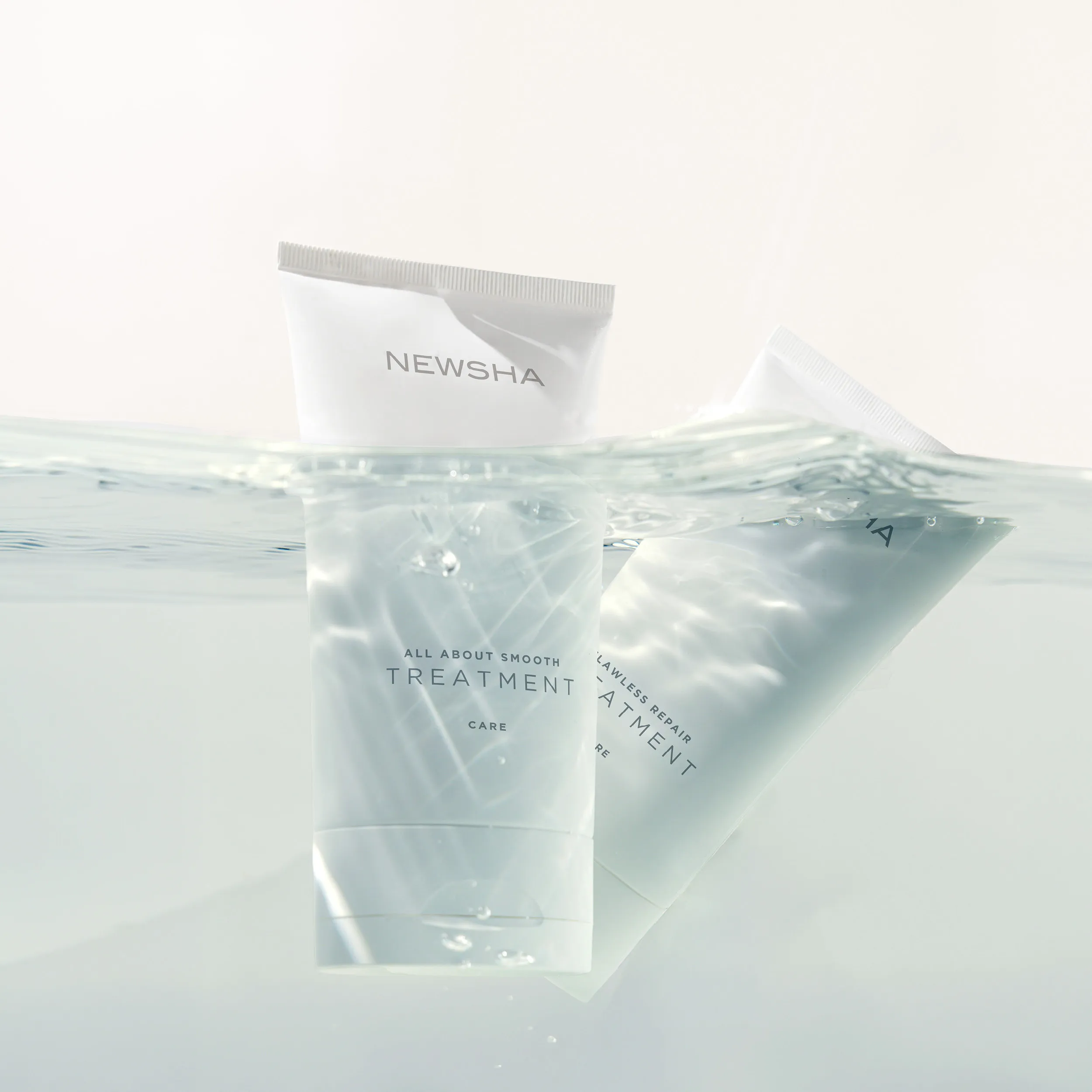Zwei NEWSHA Treatment Tuben teilweise unter Wasser mit sanften Lichtreflexionen und transparenter Wasseroberfl&auml;che vor hellem Hintergrund.
