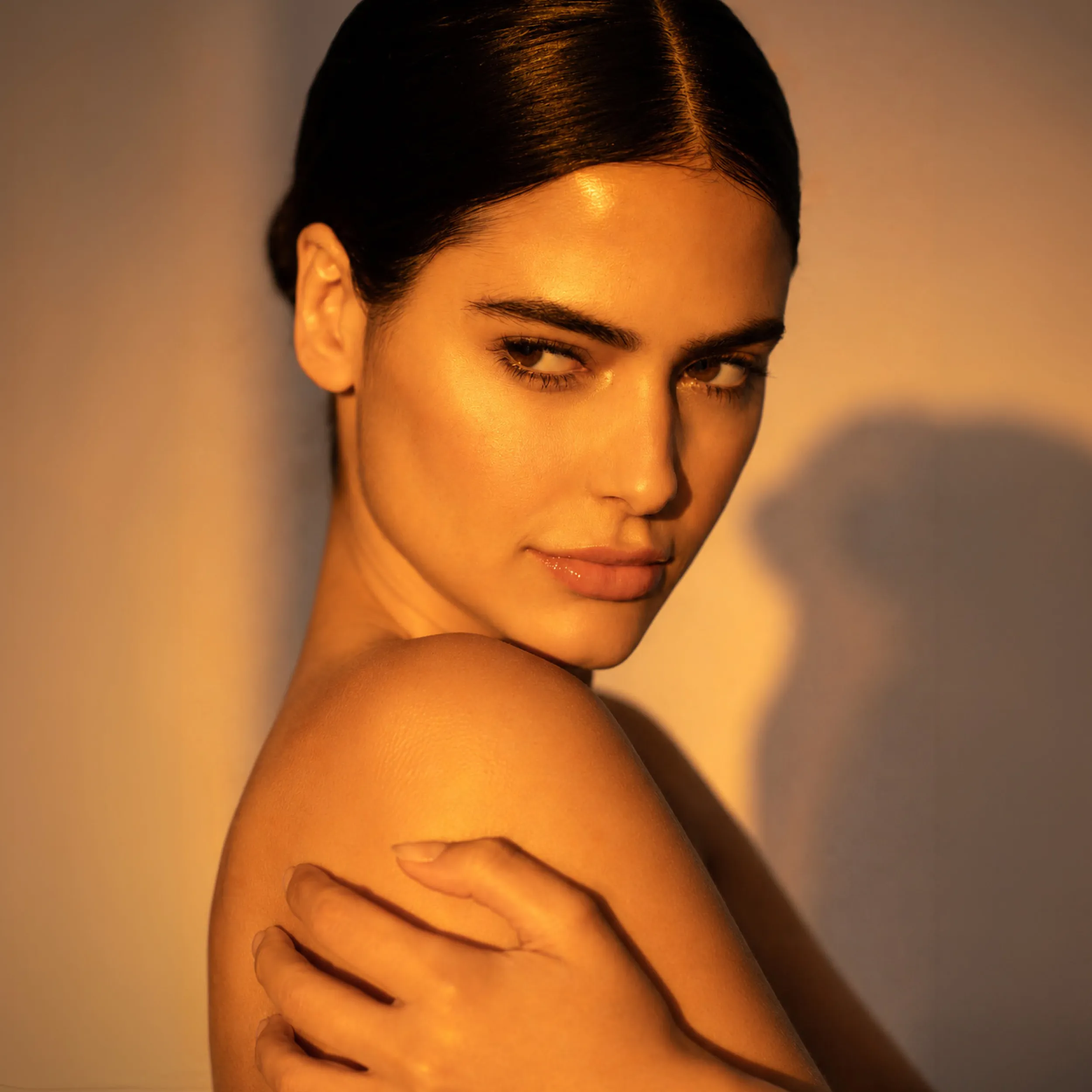 Beauty-Porträt einer Frau mit sleek zurückgebundenem Haar und warmem Golden-Hour-Licht auf strahlender Haut.
