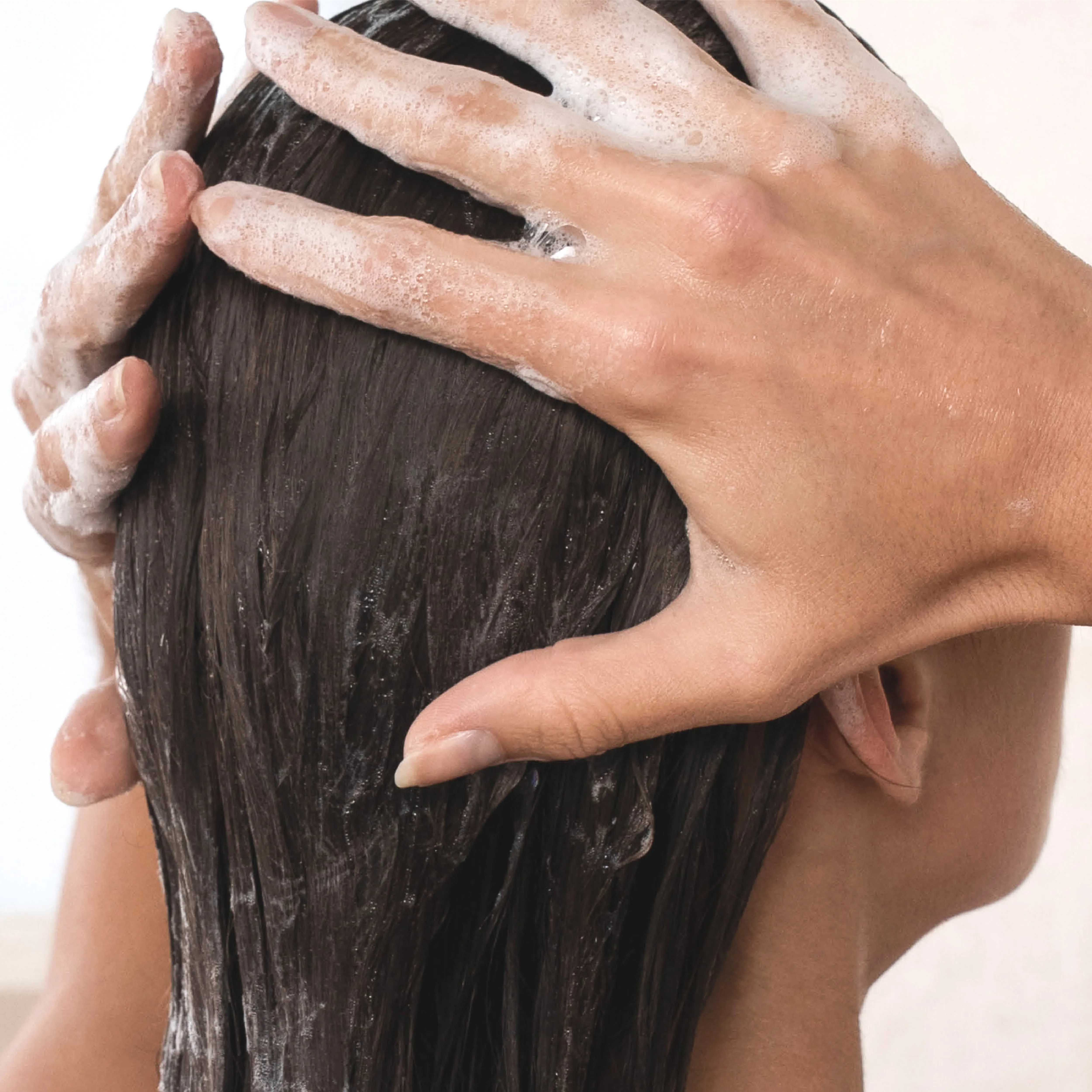 Eine Frau massiert Shampoo in die Kopfhaut ein und reinigt ihr Haar gründlich während der Haarwäsche.